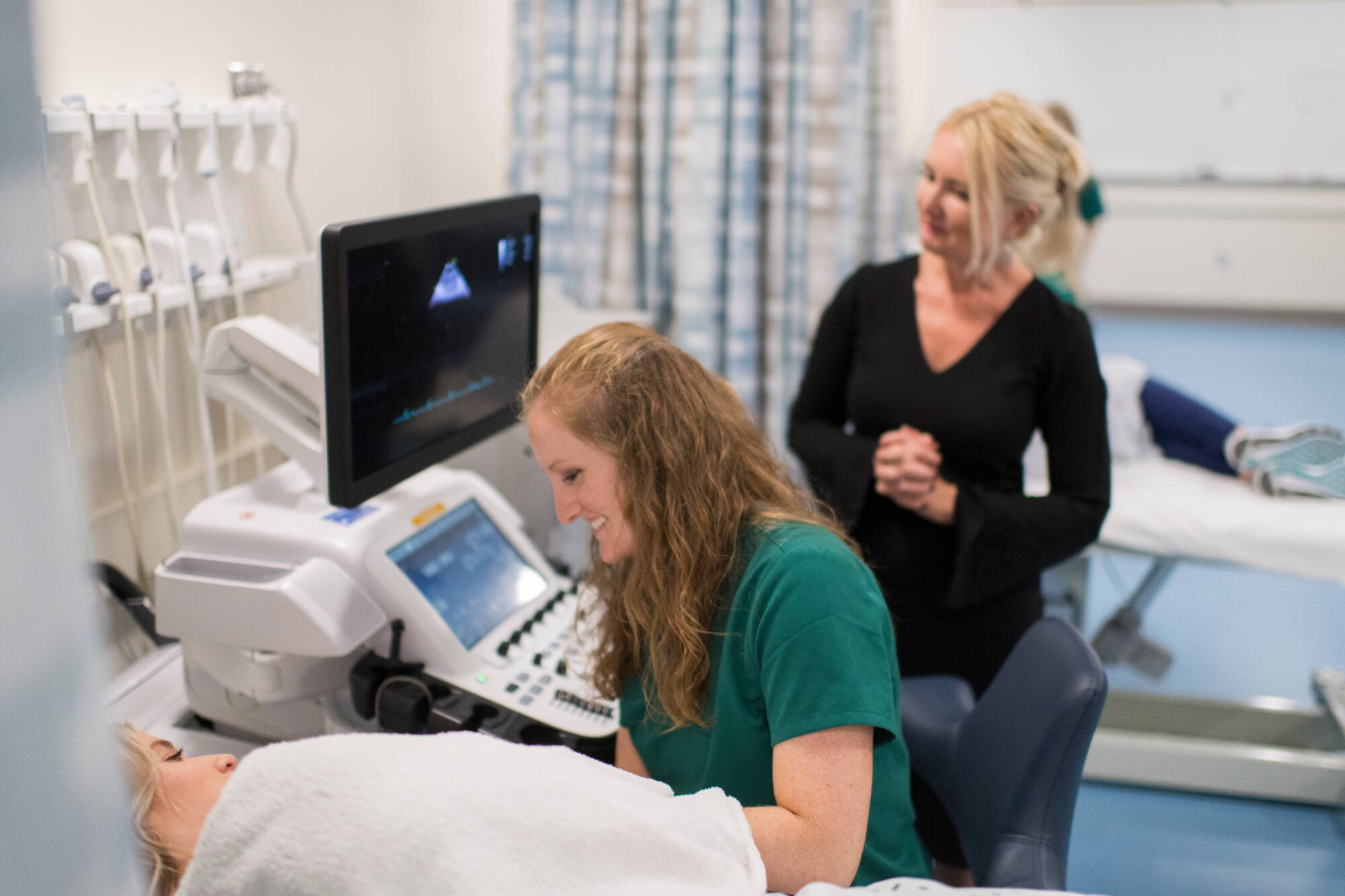 A student interacts with a manikin under the watch of their professor
